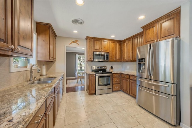 kitchen with stainless steel appliances, sink, light tile patterned floors, and light stone countertops