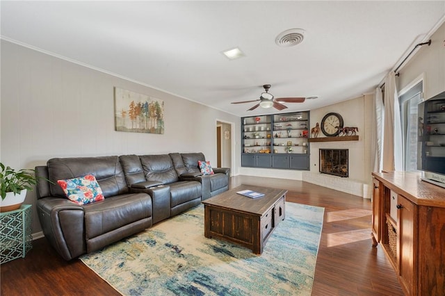 living room featuring built in shelves, ceiling fan, a brick fireplace, and dark hardwood / wood-style flooring