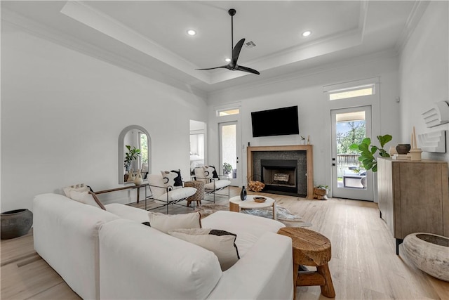 living room featuring a raised ceiling, ornamental molding, ceiling fan, and light wood-type flooring