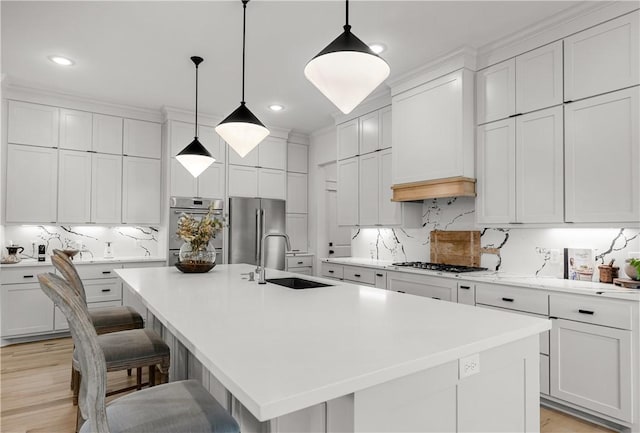 kitchen featuring appliances with stainless steel finishes, white cabinetry, sink, hanging light fixtures, and a center island with sink