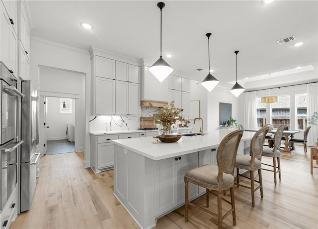 kitchen featuring tasteful backsplash, an island with sink, hanging light fixtures, and white cabinets