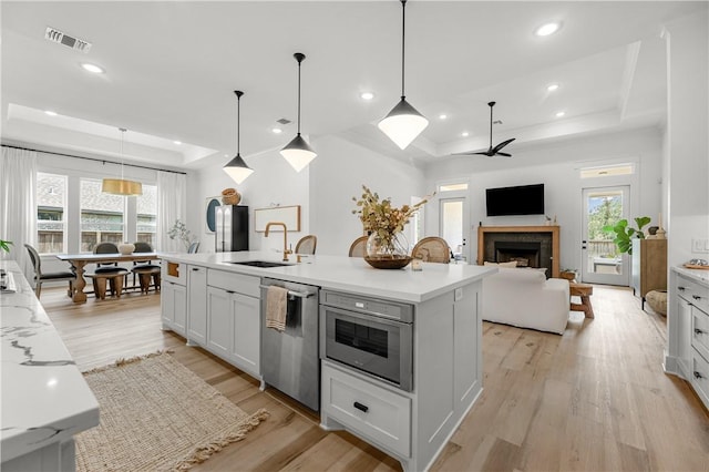 kitchen with pendant lighting, a raised ceiling, dishwasher, and a center island with sink