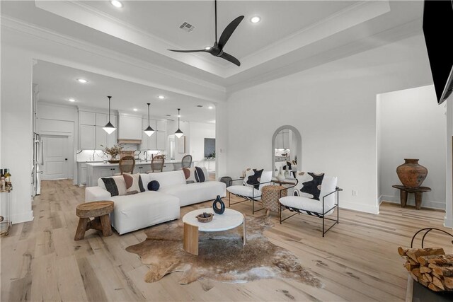 living room featuring ceiling fan, ornamental molding, a raised ceiling, and light wood-type flooring