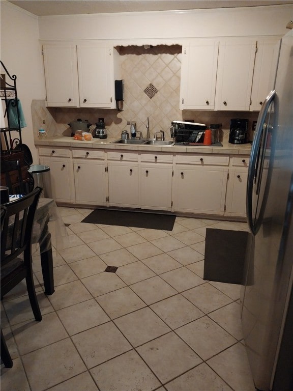 kitchen featuring sink, backsplash, white cabinets, and stainless steel refrigerator