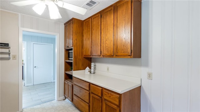 1002 Edgewood Dr, Bryan, TX 77802 - kitchen with brown cabinets, a ceiling fan, light countertops, stainless steel microwave, and light floors