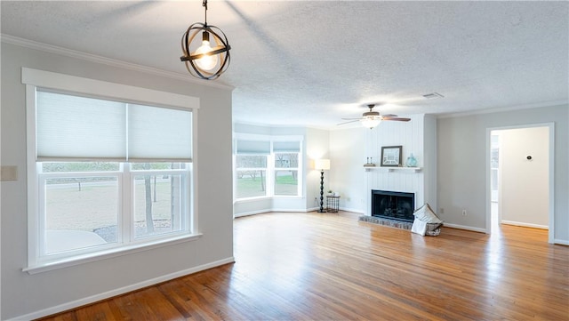 1002 Edgewood Dr, Bryan, TX 77802 - unfurnished living room featuring a textured ceiling, crown molding, wood finished floors, a fireplace with raised hearth, and ceiling fan