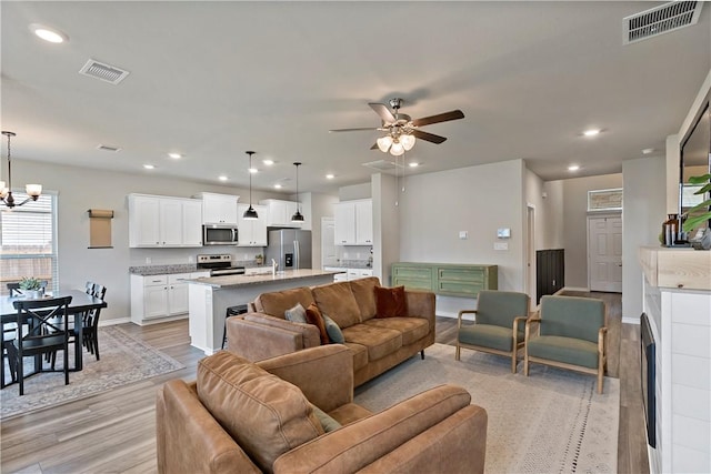 living room featuring ceiling fan with notable chandelier, light hardwood / wood-style flooring, and sink