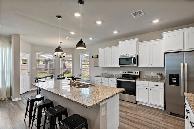 kitchen featuring white cabinets, light hardwood / wood-style flooring, an island with sink, and appliances with stainless steel finishes