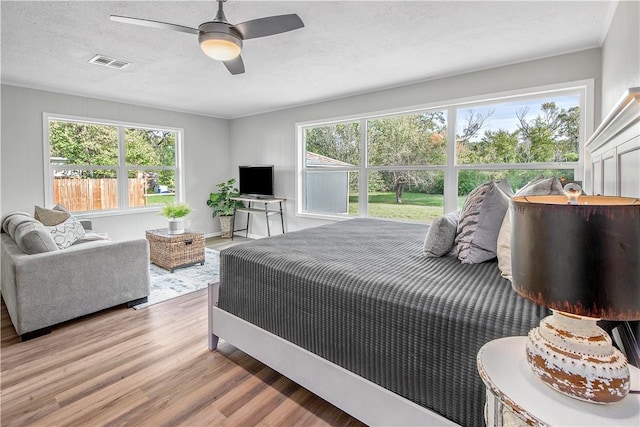 bedroom featuring multiple windows, ceiling fan, wood-type flooring, and a textured ceiling