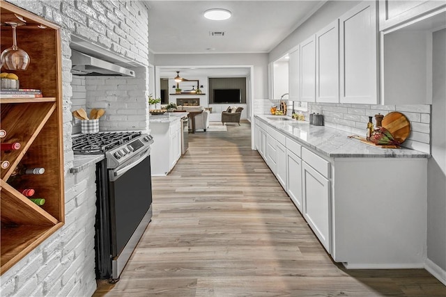 kitchen featuring stainless steel range with gas cooktop, white cabinets, and wall chimney range hood