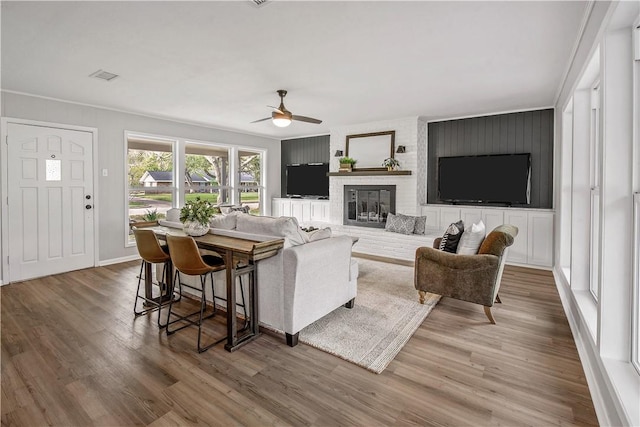 living room with a fireplace, hardwood / wood-style flooring, ceiling fan, and ornamental molding