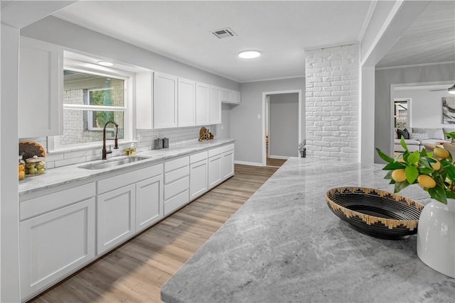 kitchen with light stone counters, white cabinetry, sink, and light hardwood / wood-style flooring