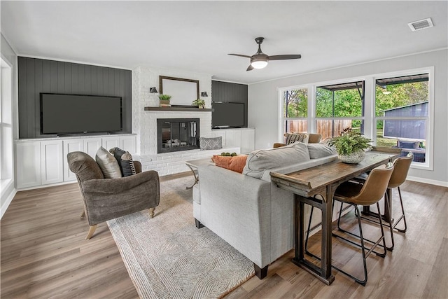 living room featuring light wood-type flooring, a brick fireplace, ceiling fan, and crown molding