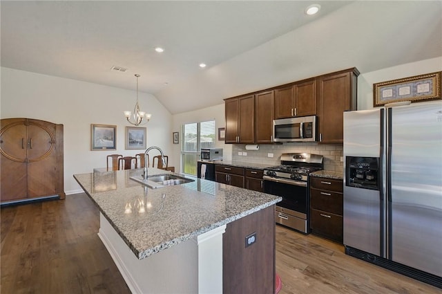 kitchen featuring light stone countertops, stainless steel appliances, a kitchen island with sink, pendant lighting, and lofted ceiling