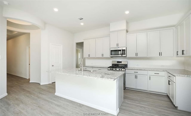 kitchen with appliances with stainless steel finishes, sink, light hardwood / wood-style floors, white cabinetry, and an island with sink