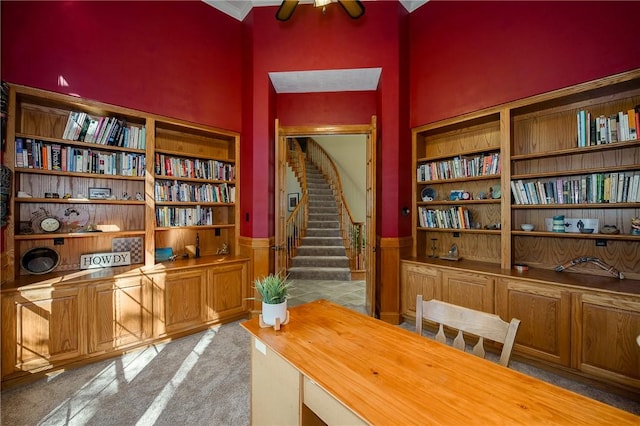 carpeted office featuring built in shelves, ceiling fan, and a towering ceiling