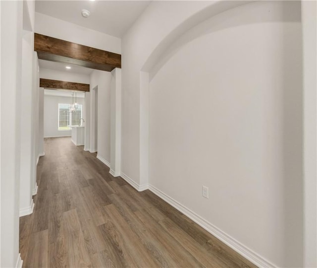 hall with hardwood / wood-style floors, beamed ceiling, and a notable chandelier