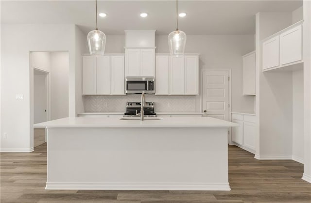 kitchen featuring a kitchen island with sink, stainless steel appliances, and decorative light fixtures