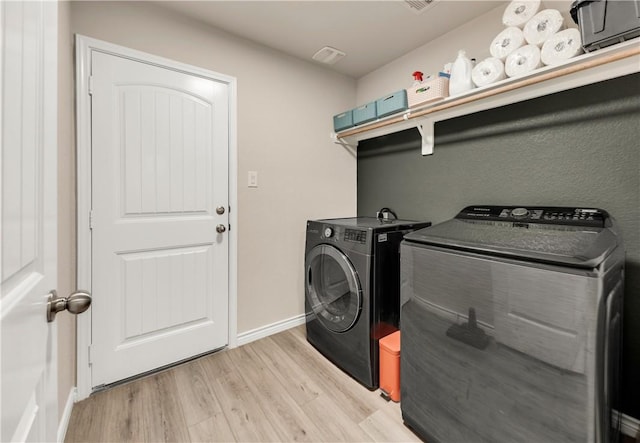 laundry room featuring washing machine and clothes dryer and light hardwood / wood-style flooring