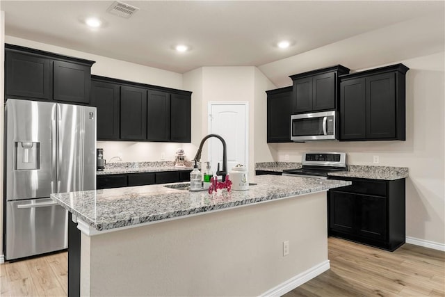 kitchen with stainless steel appliances, light hardwood / wood-style flooring, and a center island with sink