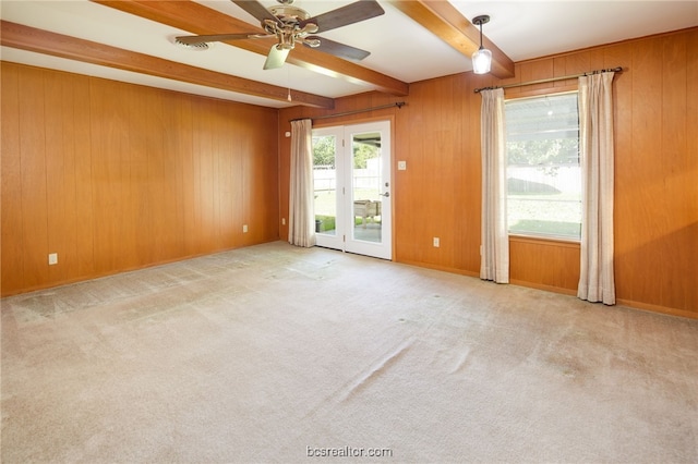 carpeted spare room featuring ceiling fan, beam ceiling, and wooden walls