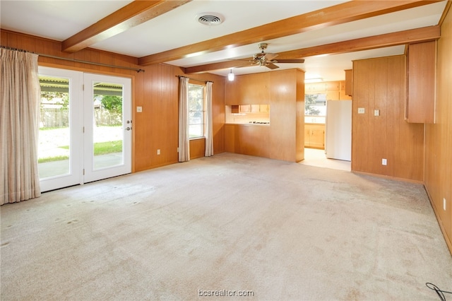 unfurnished living room featuring beamed ceiling, ceiling fan, wood walls, and light carpet