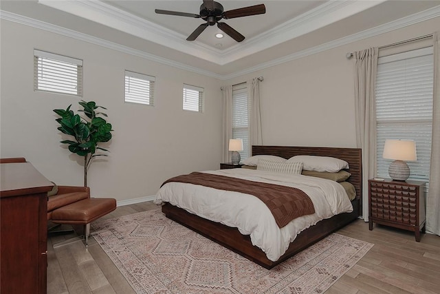 bedroom with crown molding, a tray ceiling, and light hardwood / wood-style flooring