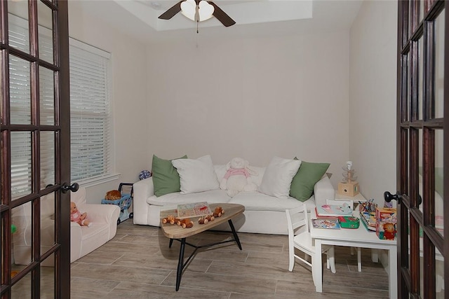 living room featuring a raised ceiling, light hardwood / wood-style flooring, ceiling fan, and french doors