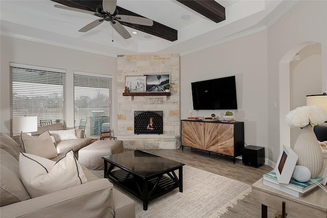 living room featuring crown molding, a stone fireplace, beam ceiling, and light hardwood / wood-style flooring