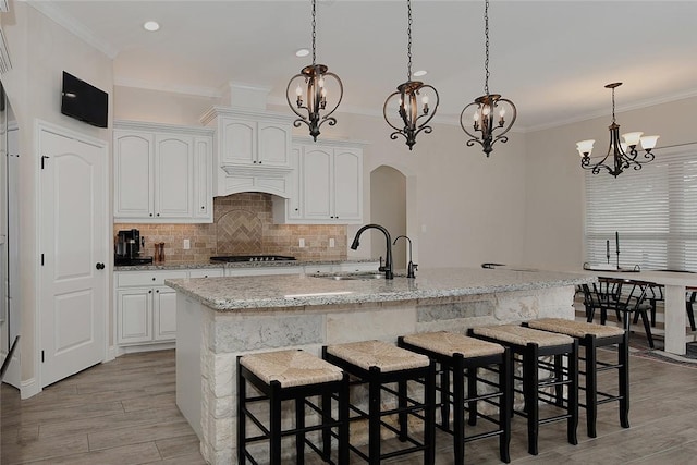 kitchen with decorative light fixtures, an island with sink, sink, white cabinets, and light stone countertops