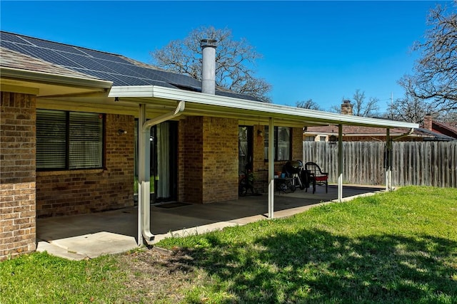 exterior space with a patio, roof mounted solar panels, fence, a yard, and brick siding