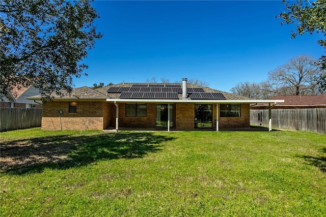 rear view of house featuring brick siding, a fenced backyard, a lawn, and roof mounted solar panels