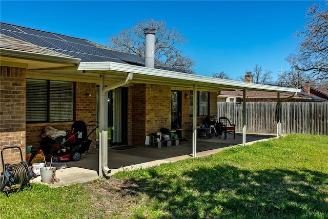 rear view of property with a patio, fence, solar panels, a yard, and brick siding