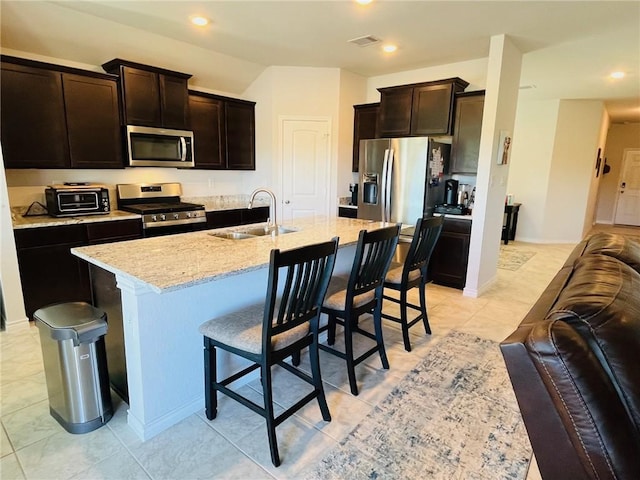 kitchen with a center island with sink, a kitchen breakfast bar, sink, dark brown cabinets, and stainless steel appliances