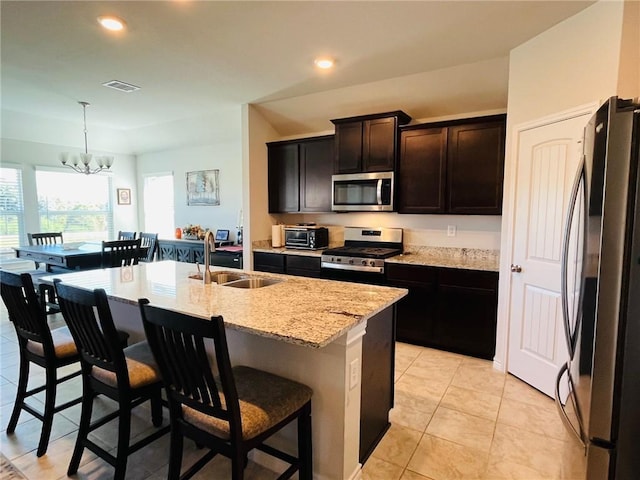 kitchen with appliances with stainless steel finishes, a kitchen island with sink, sink, an inviting chandelier, and hanging light fixtures