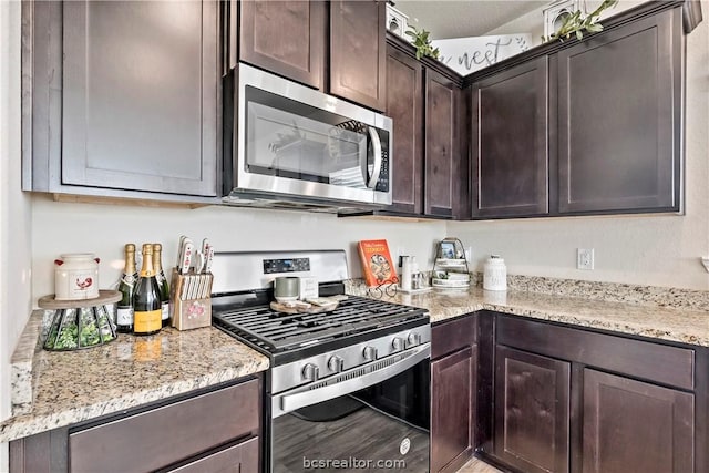 kitchen with dark brown cabinetry, light stone countertops, and stainless steel appliances