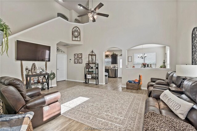 living room with ceiling fan with notable chandelier, wood-type flooring, and a high ceiling