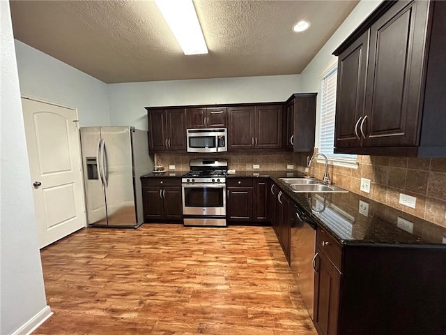 kitchen with light wood-type flooring, dark stone counters, dark brown cabinetry, stainless steel appliances, and sink