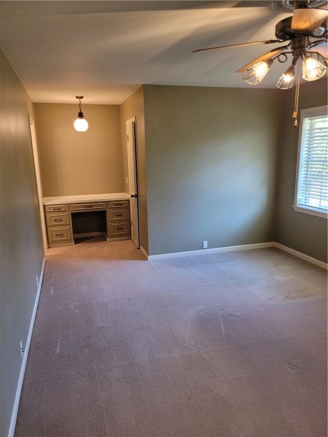 carpeted spare room with built in desk and ceiling fan