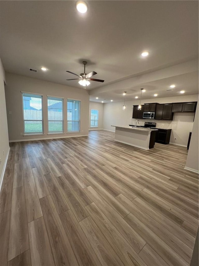 unfurnished living room with ceiling fan, sink, and light wood-type flooring