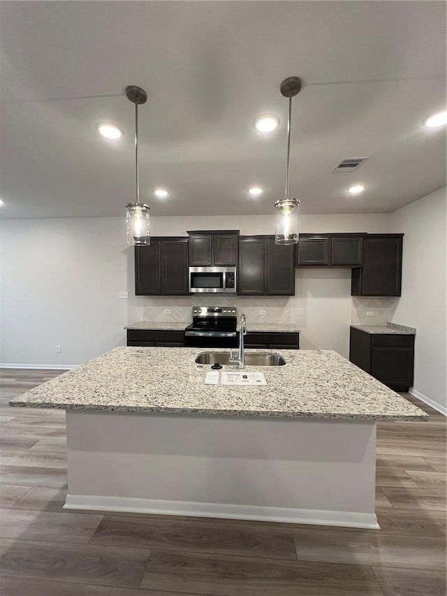 kitchen with wood-type flooring, appliances with stainless steel finishes, pendant lighting, and an island with sink