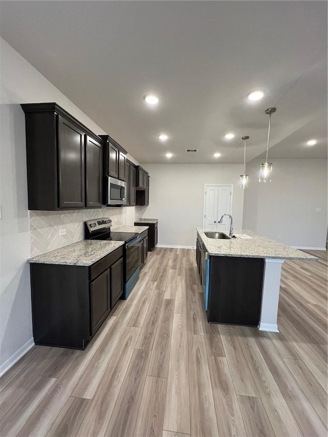 kitchen with light stone countertops, appliances with stainless steel finishes, light wood-type flooring, sink, and pendant lighting