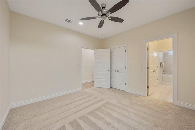 unfurnished bedroom with ceiling fan, light colored carpet, a closet, and ensuite bath