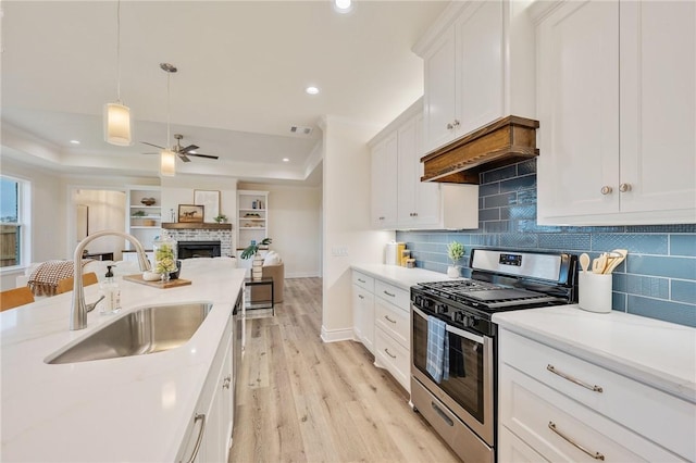 kitchen featuring sink, stainless steel range with gas cooktop, white cabinetry, and a tray ceiling