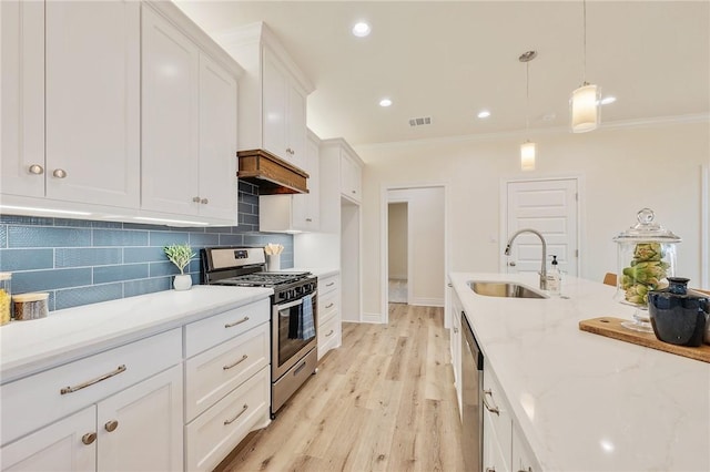 kitchen with appliances with stainless steel finishes, white cabinetry, sink, hanging light fixtures, and light wood-type flooring