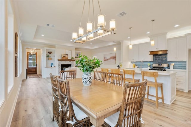 dining space featuring light hardwood / wood-style flooring, a raised ceiling, a fireplace, ornamental molding, and a chandelier