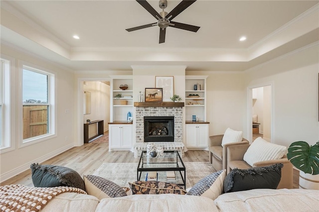 living room featuring crown molding, light hardwood / wood-style flooring, a raised ceiling, and a fireplace