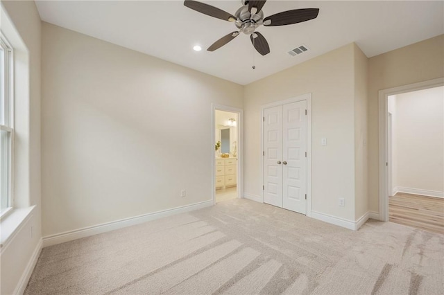 unfurnished bedroom with ceiling fan, light carpet, a closet, and ensuite bath