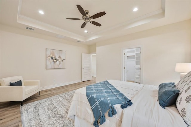 bedroom featuring a spacious closet, light hardwood / wood-style floors, a closet, a raised ceiling, and ceiling fan