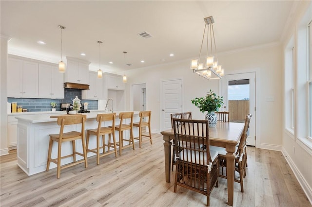 dining space with sink, light wood-type flooring, an inviting chandelier, and ornamental molding